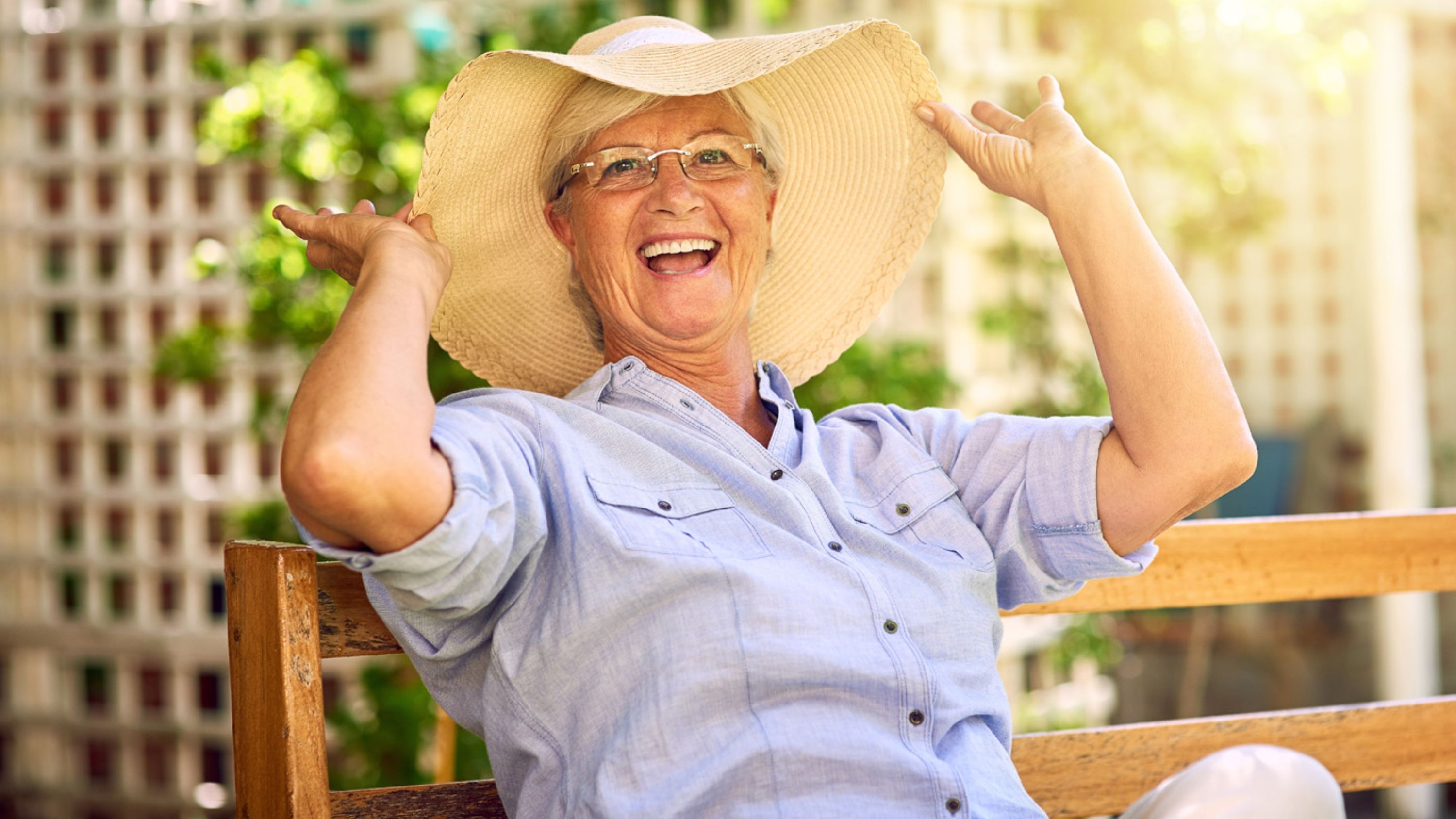 Eine ältere Dame mit Hut sitzt auf einer Bank im Sommer.