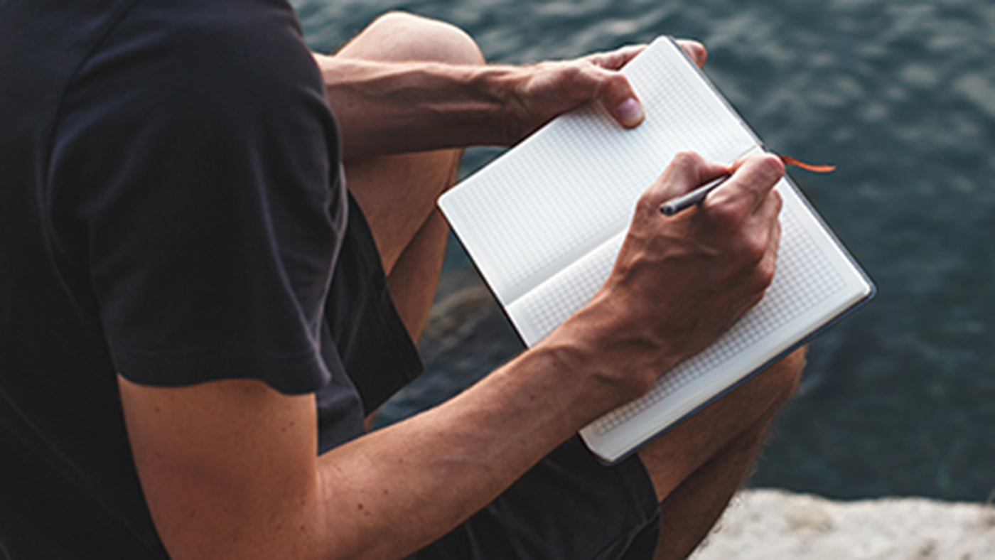 Ein Herr schreibt in sein Notizblock und schaut aufs Wasser.